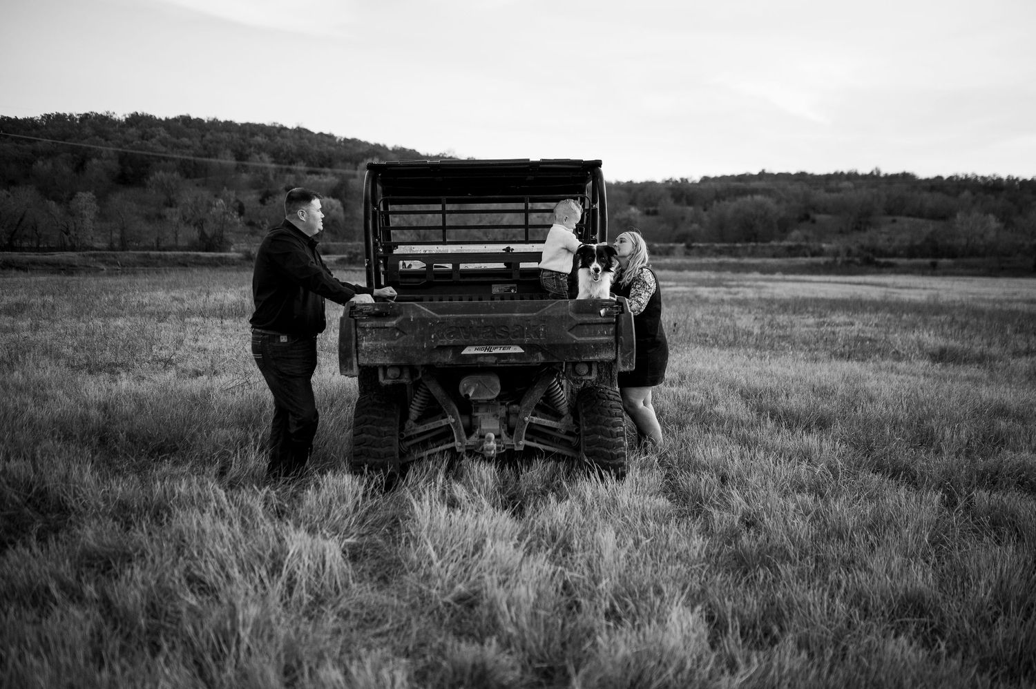 Black and white image of a family gathered around an ATV in an open rural field at dusk.