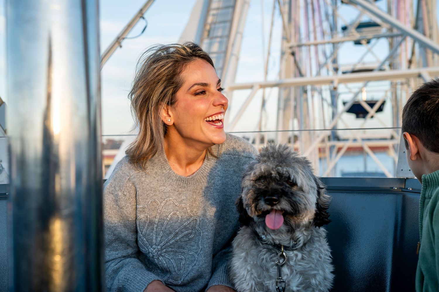 Woman smiling with fluffy dog on a Ferris wheel ride at sunset.