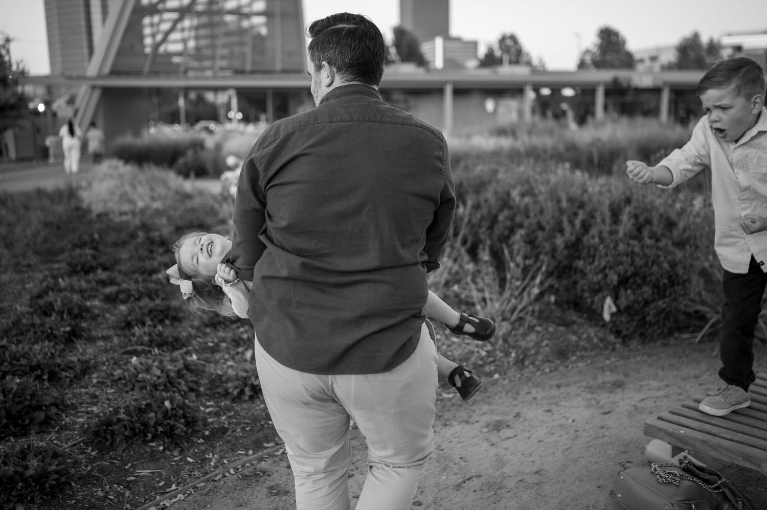 Black and white candid photo of people playing in a park near urban structures.