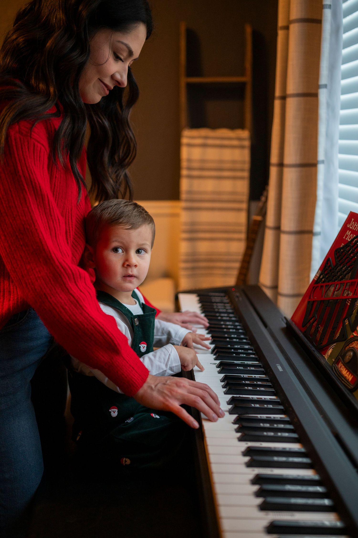 A piano lesson moment captured in warm lighting with a red sweater creating cozy atmosphere.