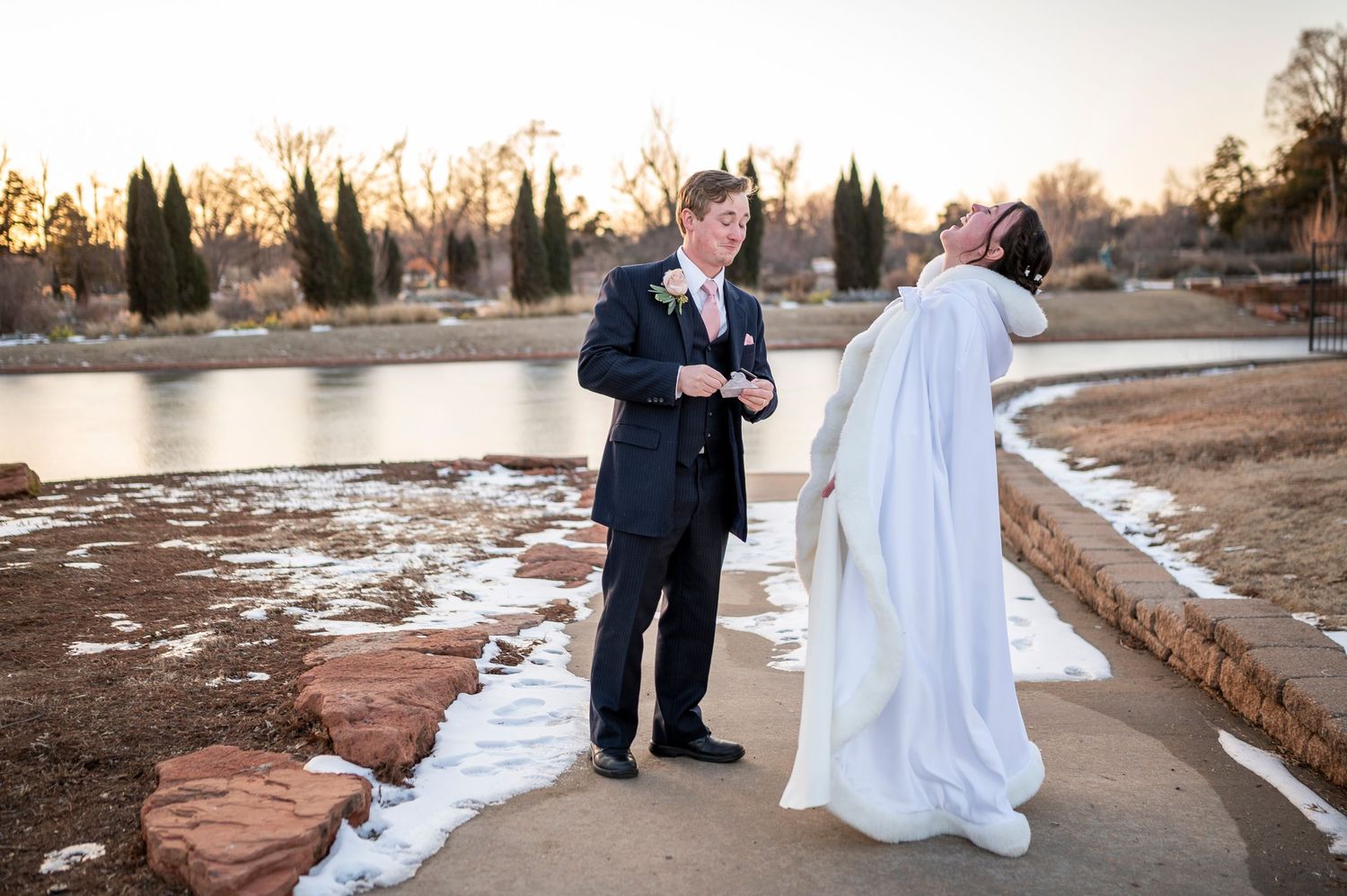 A winter wedding scene with a couple sharing a moment by a frozen lake at sunset.