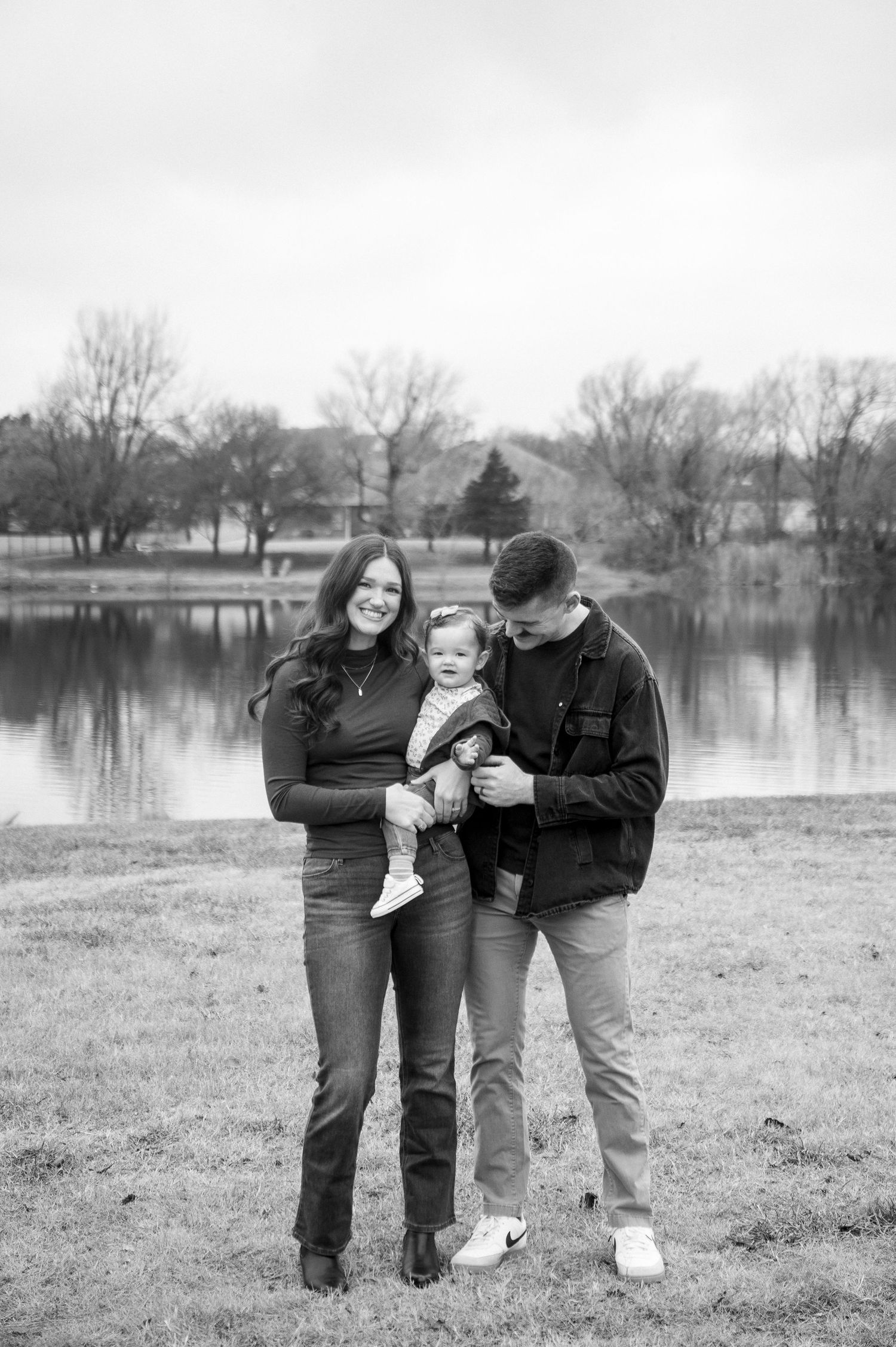 A black and white family portrait taken by a lake on an overcast day.
