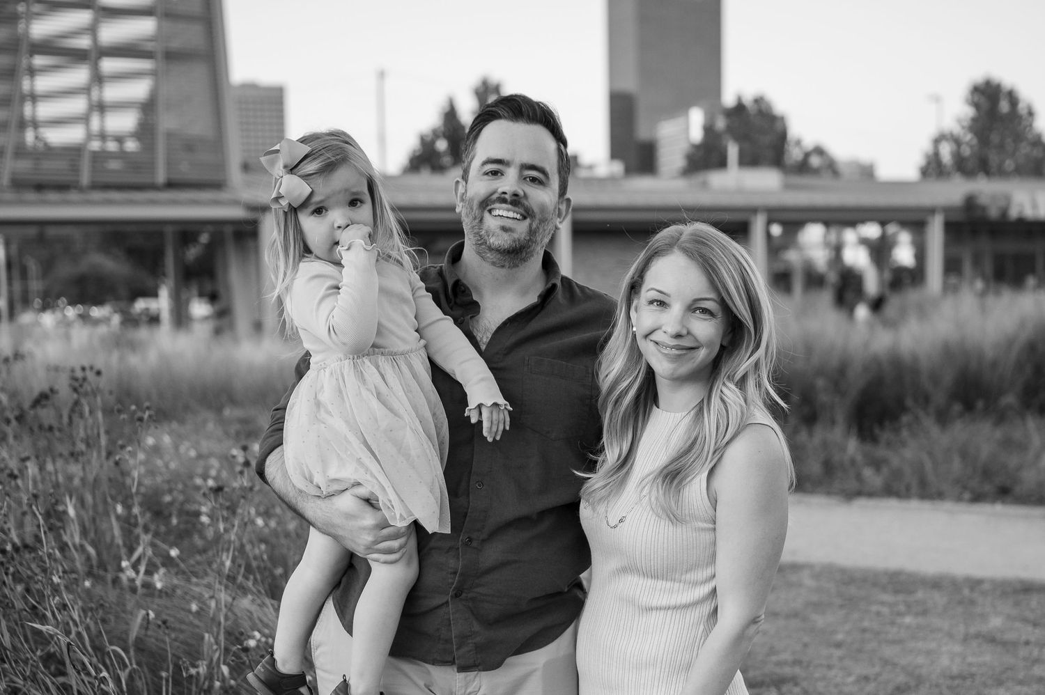 Black and white portrait of a family outdoors at sunset in an urban park setting.