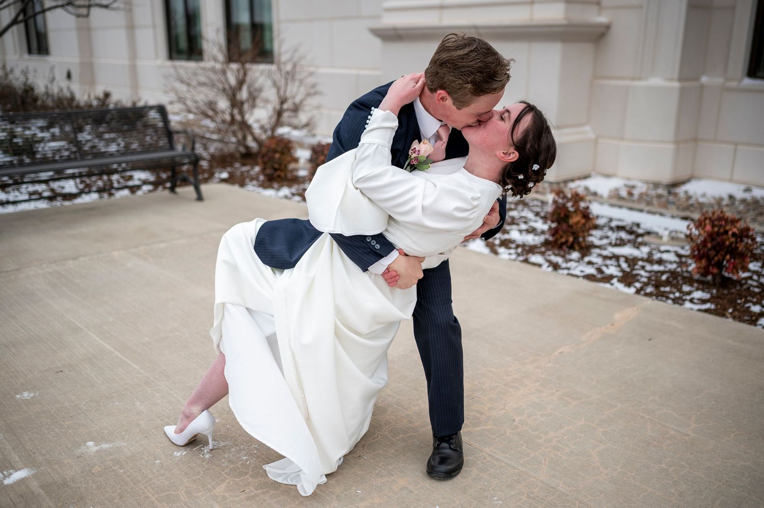 A dramatic wedding dip pose featuring formal attire and a white fur-trimmed cape against a snowy backdrop.