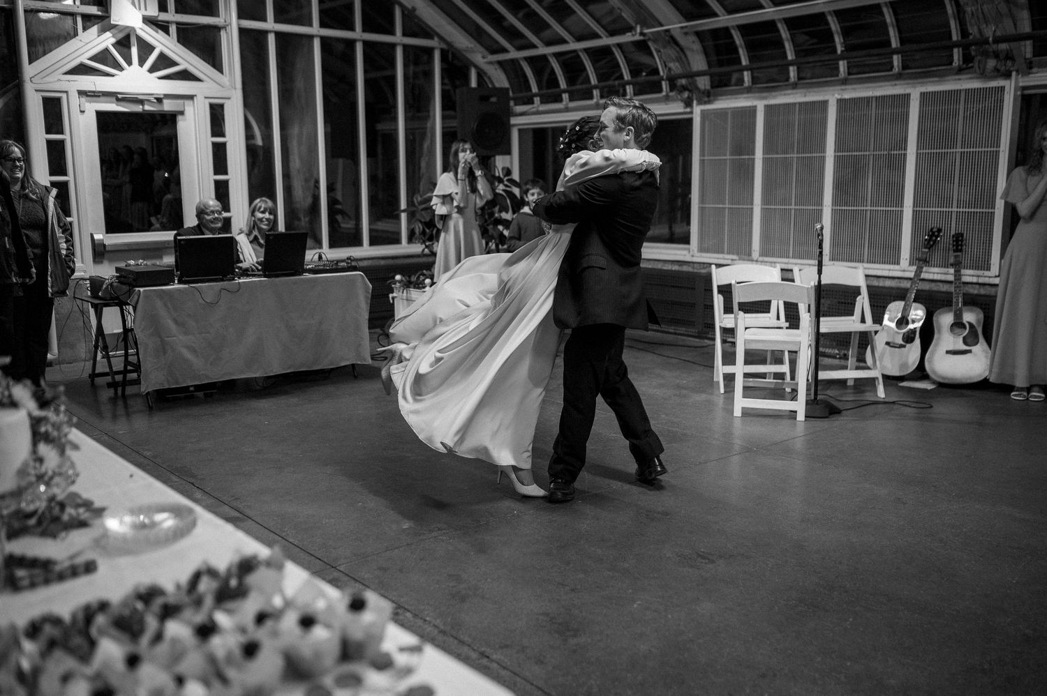 A black and white photo of a couple dancing at their wedding reception in a greenhouse.