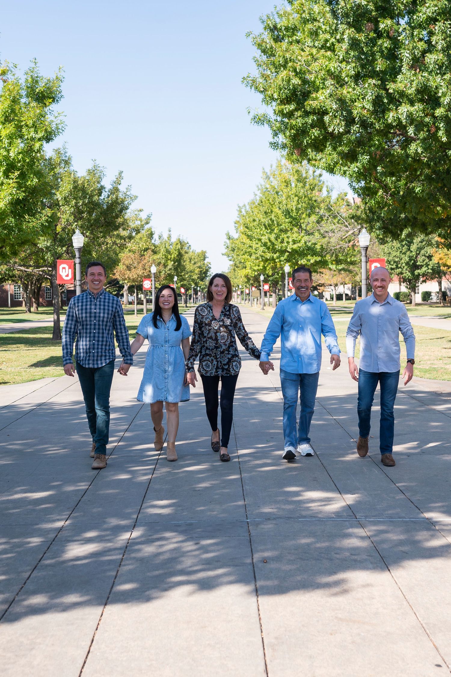 A group walks together holding hands on a tree-lined university campus pathway.
