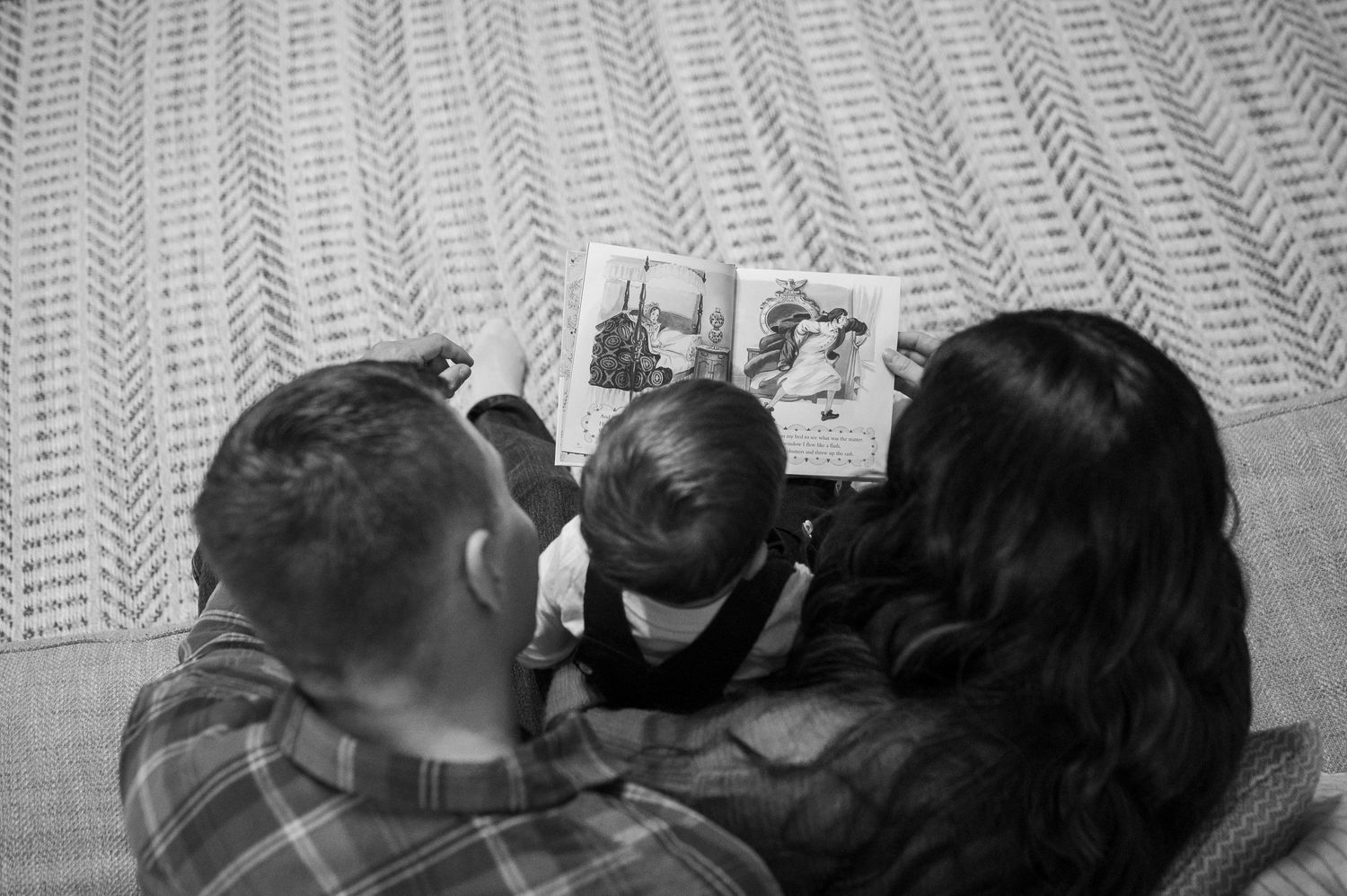 A family reads together while snuggled up on a textured blanket.