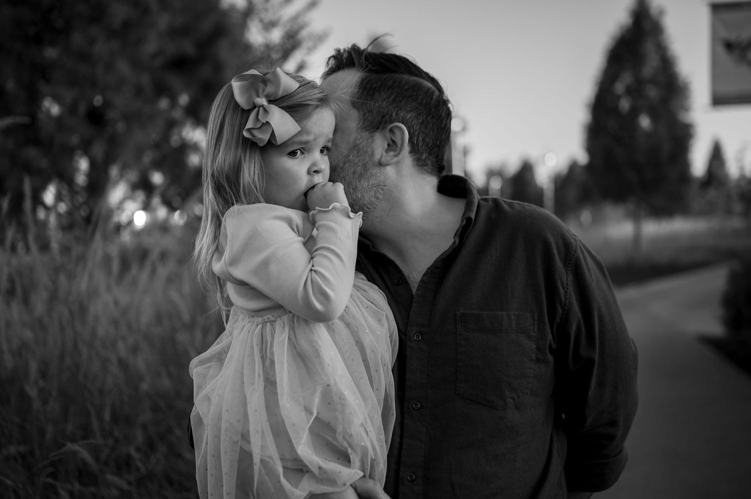 A tender moment captured in black and white between two people in an outdoor setting at dusk.