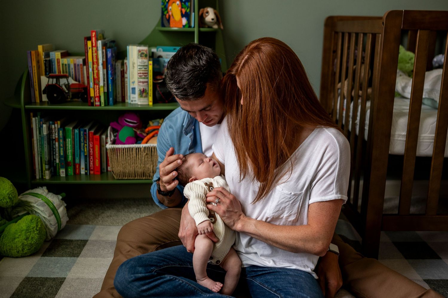 Parents sitting on floor together lovingly caring for their newborn baby in a cozy nursery room.