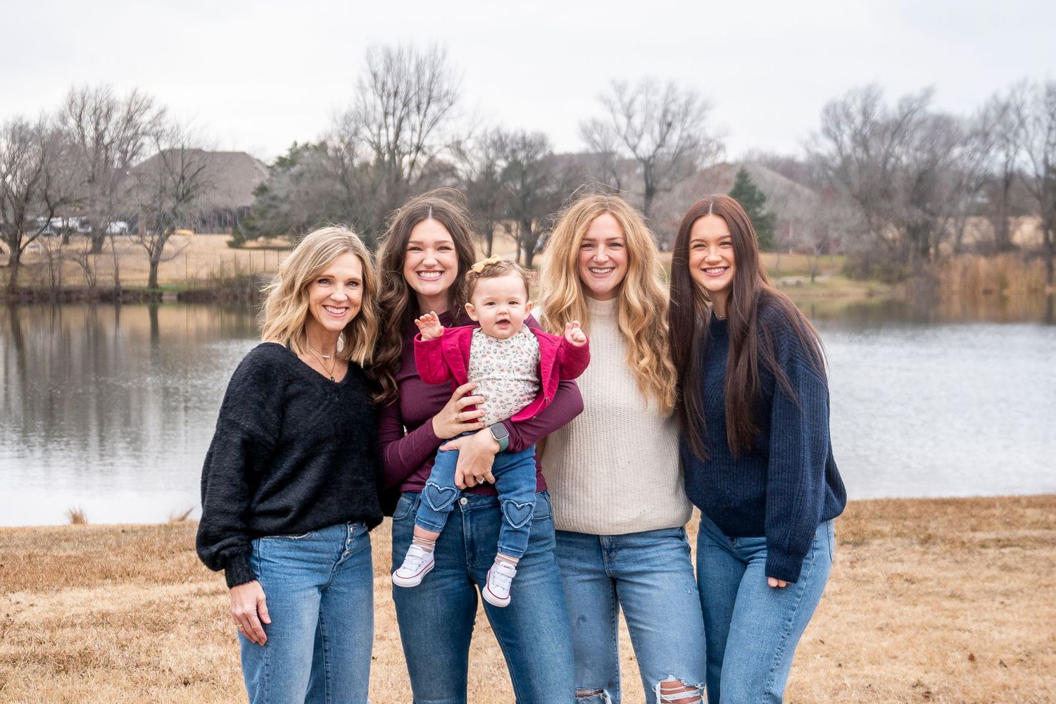 Group of women in casual attire posing together by a serene lake.