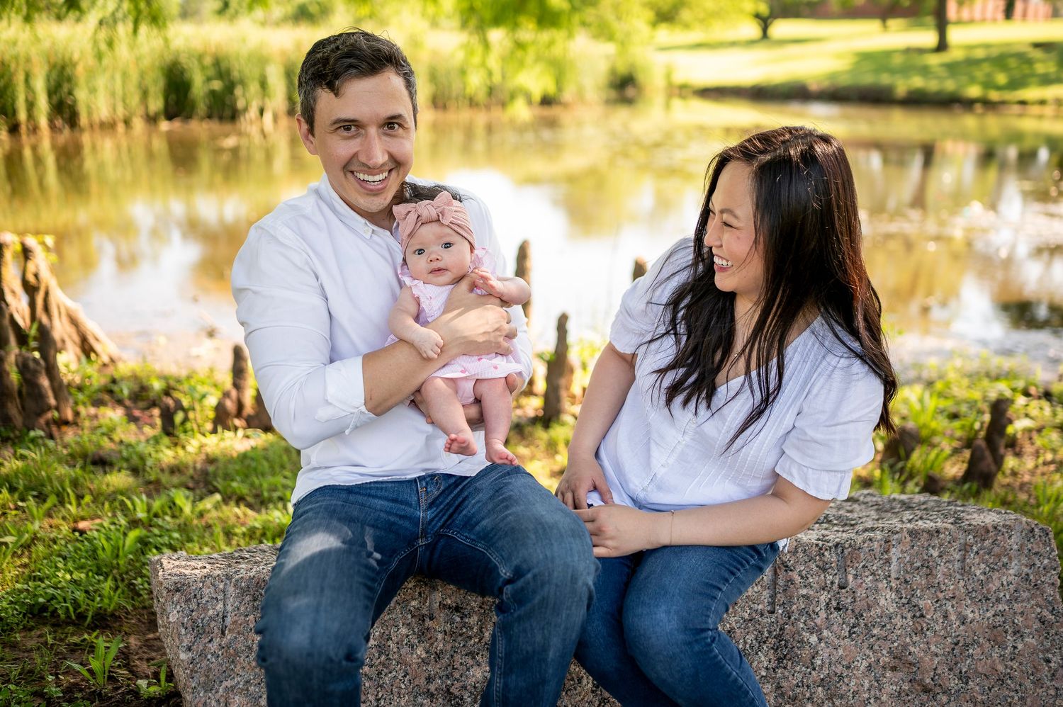 A family sits together on a stone wall near a pond on a sunny day in nature.