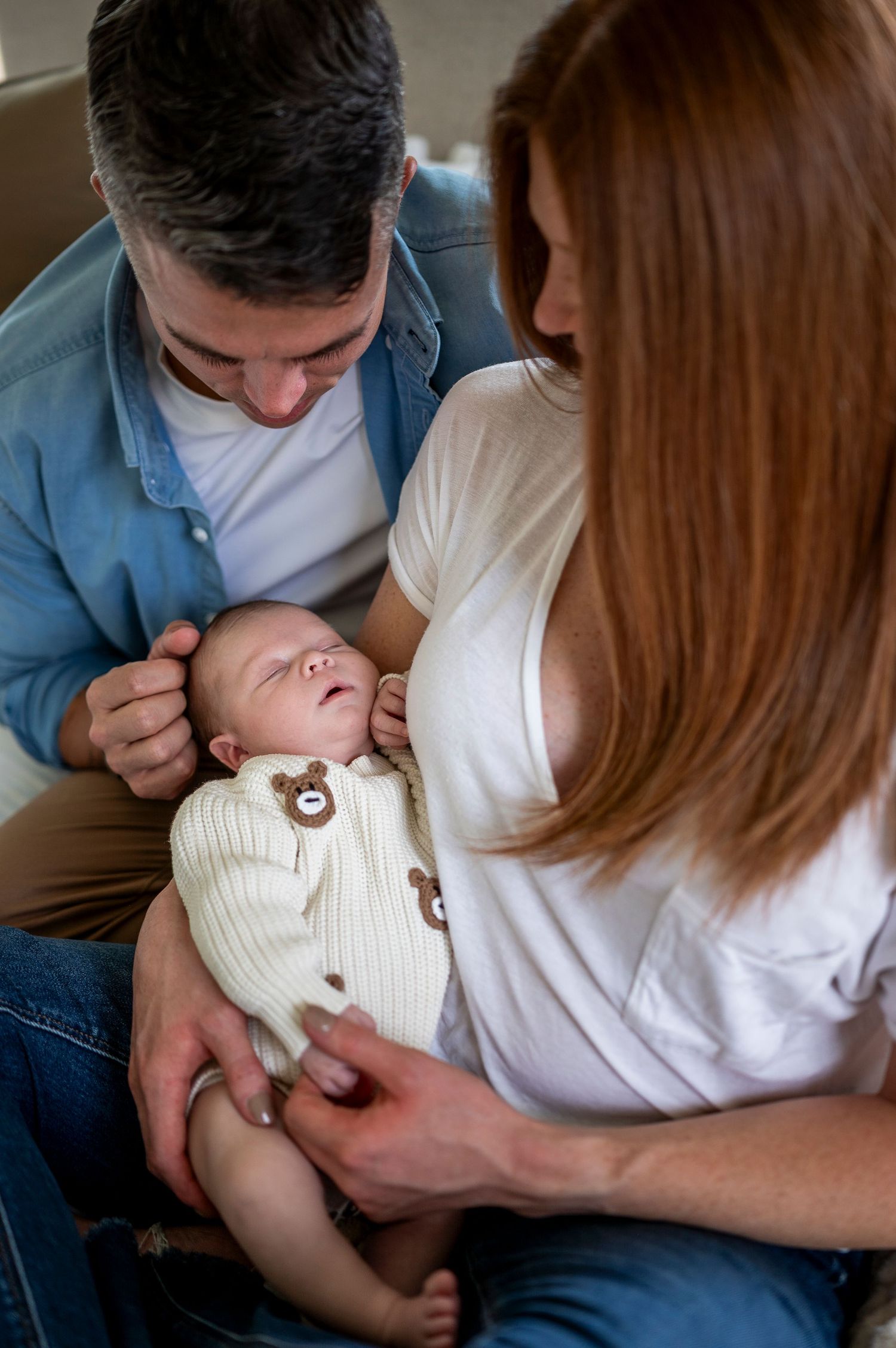 New parents lovingly cradle their sleeping newborn baby dressed in a white bear outfit.