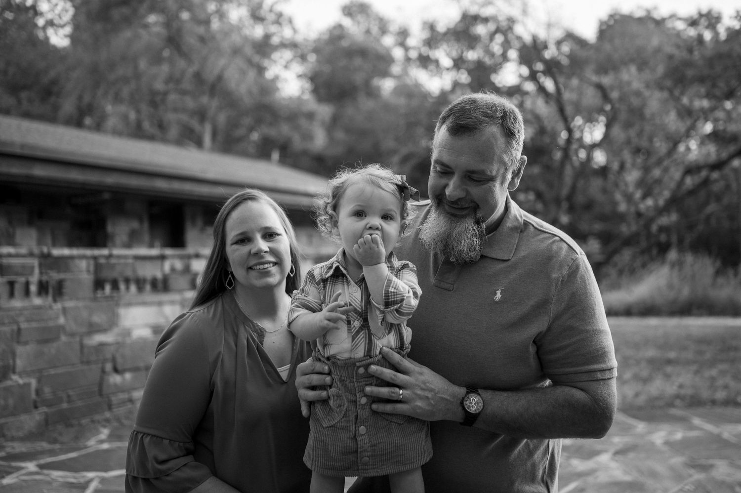 Black and white family portrait taken outdoors with rustic building in background.