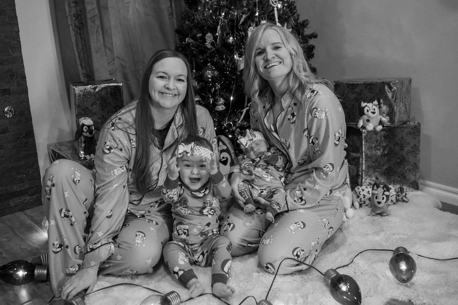 A black and white photo of a family wearing matching pajamas celebrating together by a Christmas tree.