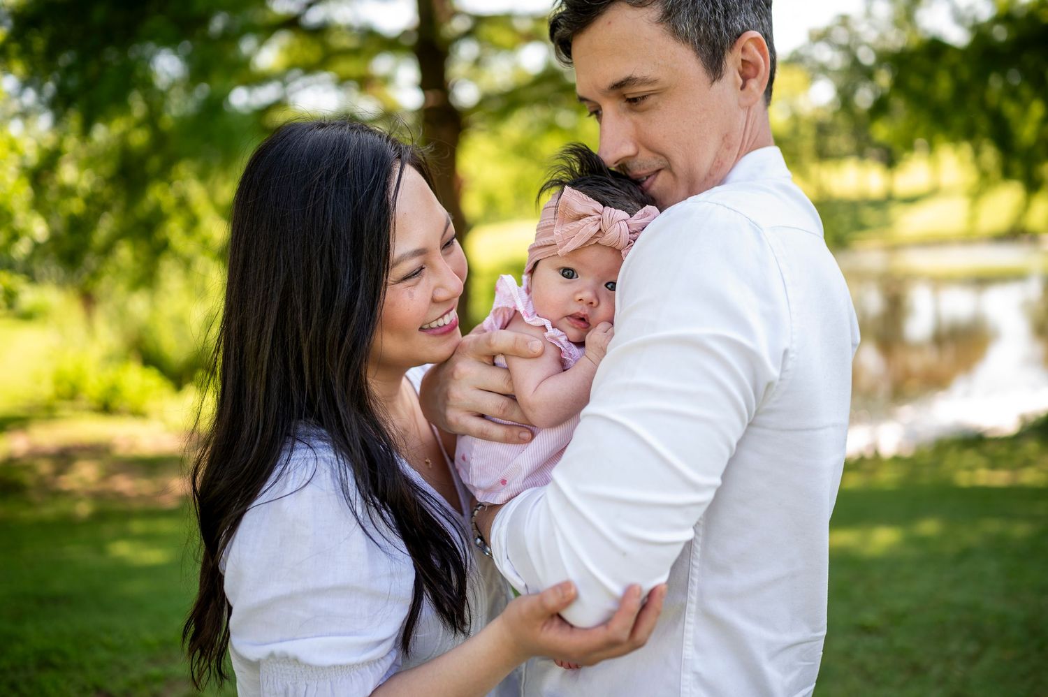 A couple shares a tender moment with their baby in a sunny park setting.