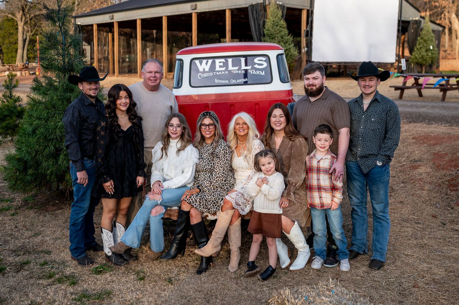 Group of people posing outdoors near a vintage Wells truck with a large screen backdrop at a festive evening gathering.