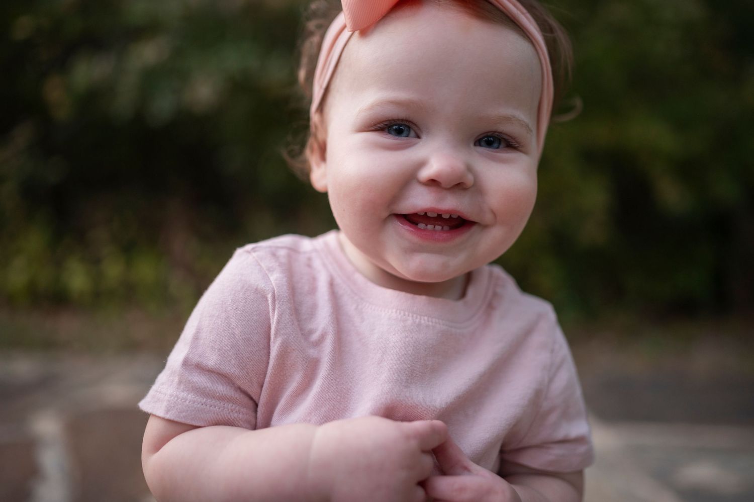 Close-up portrait of small child in pink outfit with bow smiling.