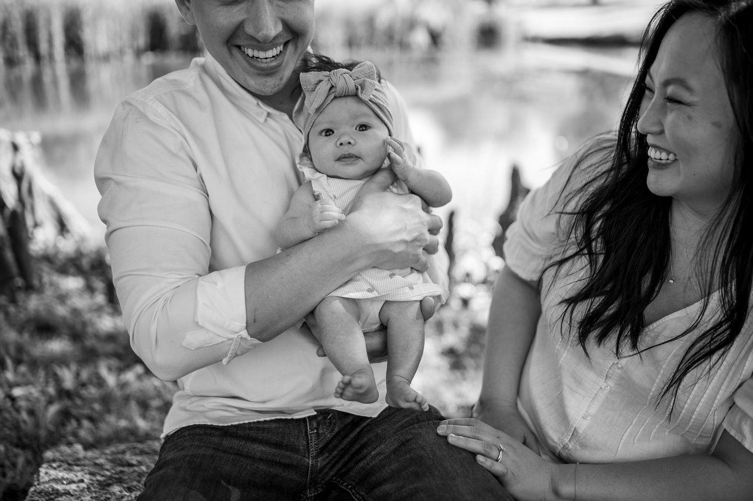 Black and white photo of a family sharing a joyful outdoor moment with their baby in a natural setting.