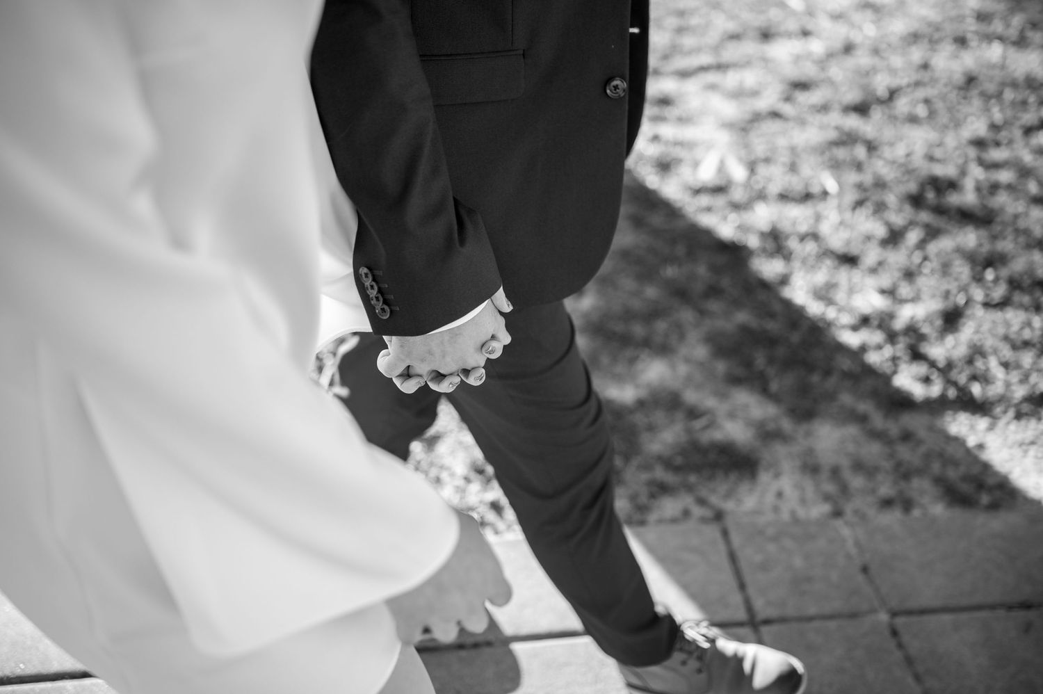 A black and white photo shows wedding attire detail with contrasting dark suit and white dress touching at ground level.