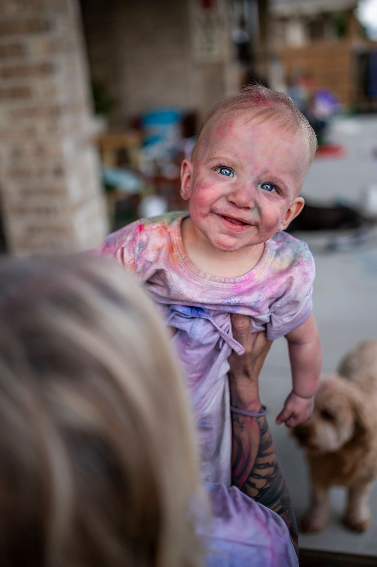 A baby wearing a purple dress sits among puppies, smiling with joy while interacting with them.