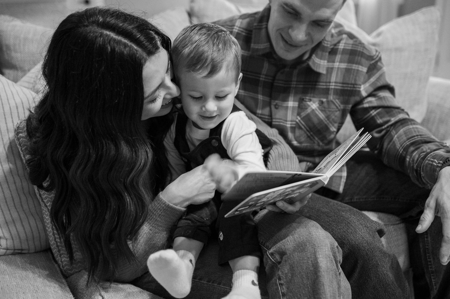 A family reads a book together while sitting on a couch in black and white.