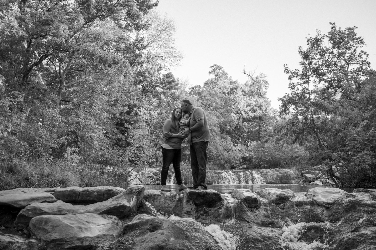 Black and white photo of a couple standing on rocky terrain near a waterfall.
