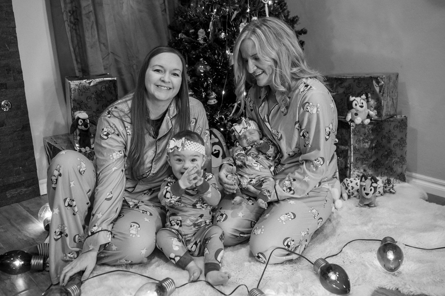 Two people wearing matching holiday pajama sets share a joyful moment in front of a Christmas tree.