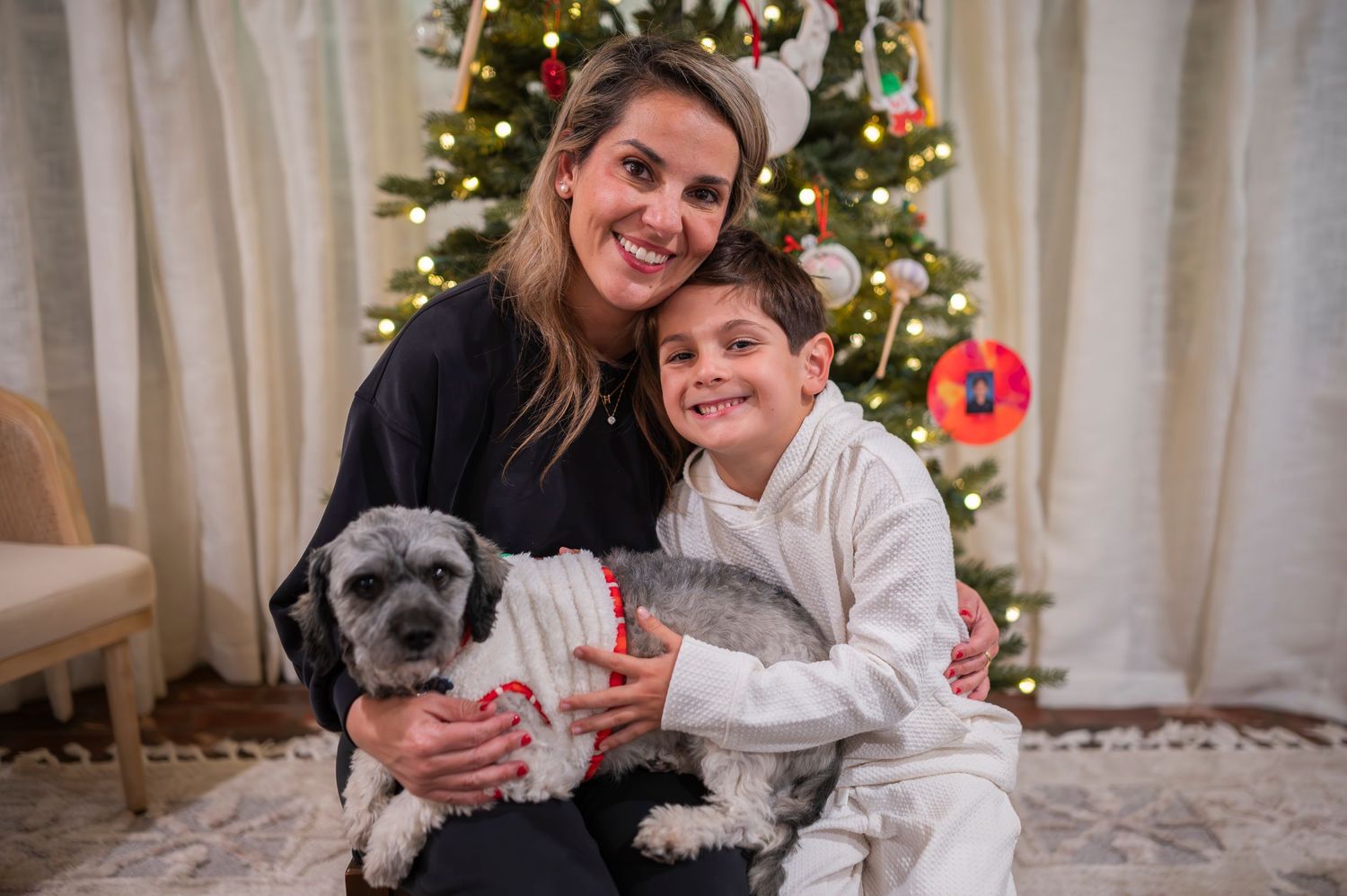 A family poses with their small grey dog in front of a decorated Christmas tree in their living room.