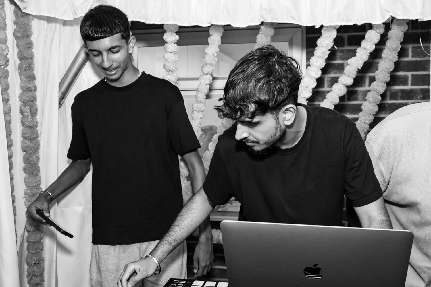 Group of DJs performing at an event with equipment and laptops in black and white.