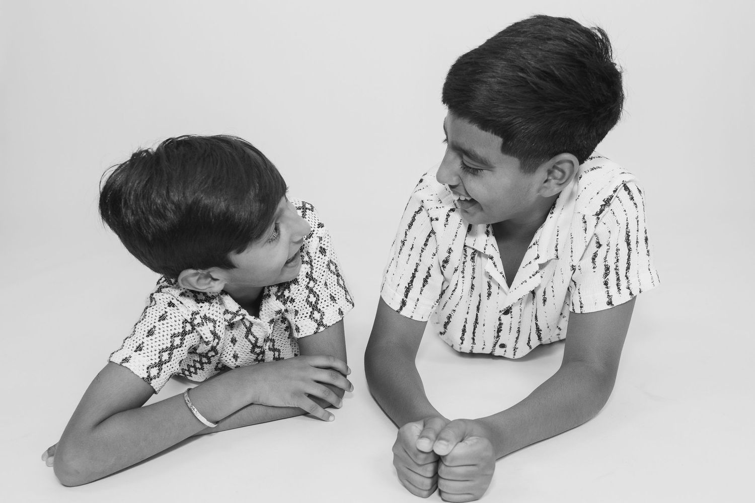 Black and white portrait of two boys in matching shirts lying down face to face.