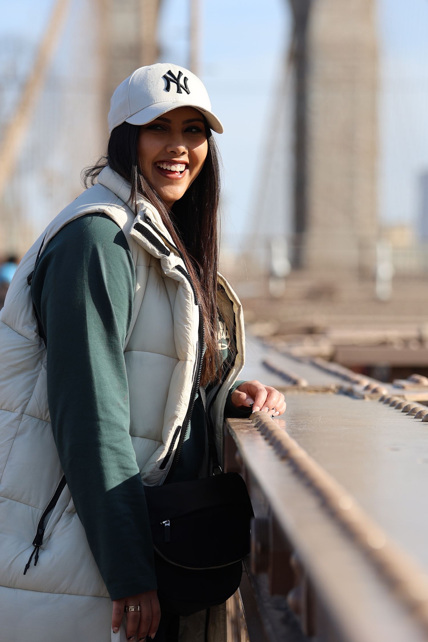 Person in baseball cap smiling on Brooklyn Bridge.