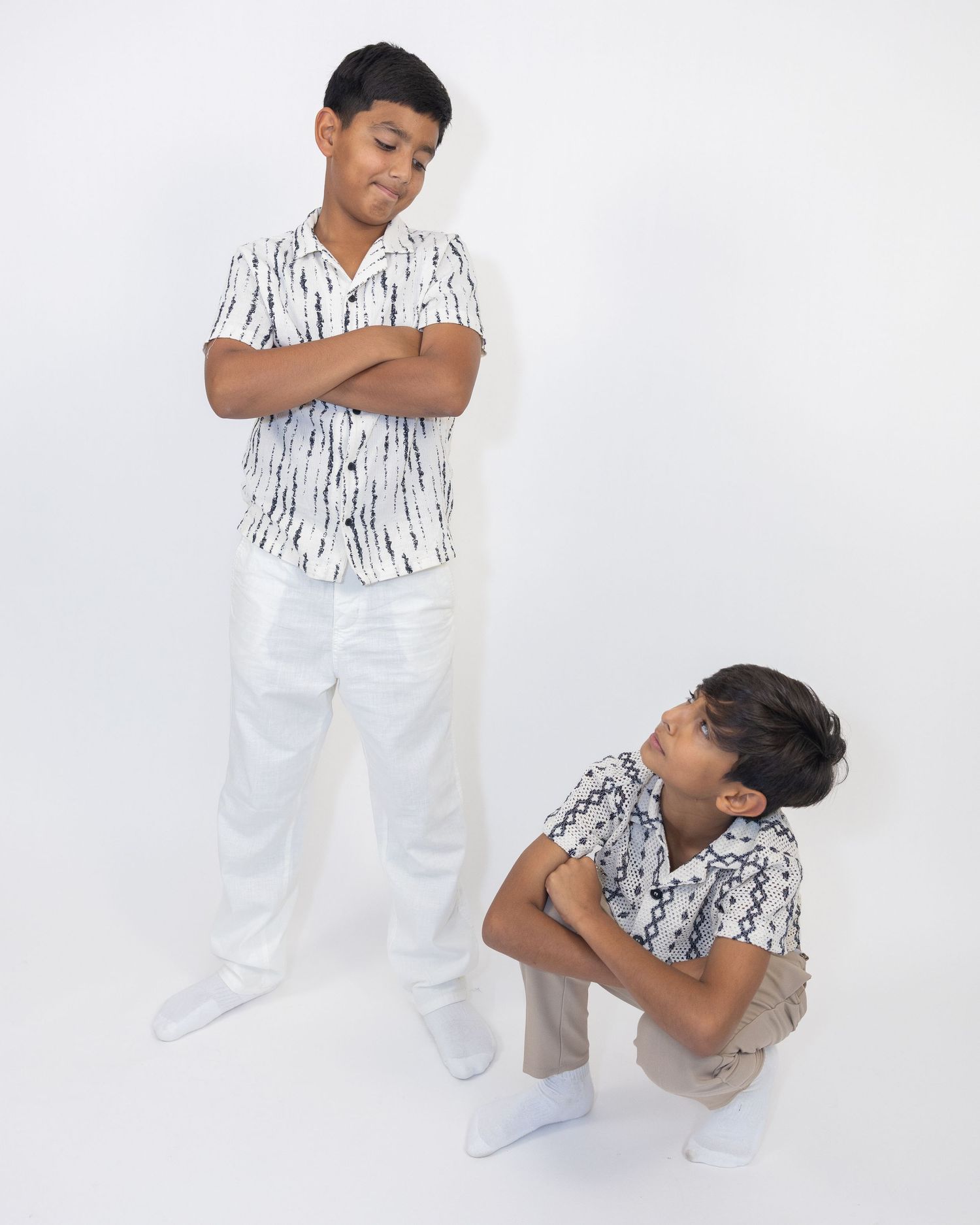 Two boys in matching patterned shirts striking playful poses against white background.
