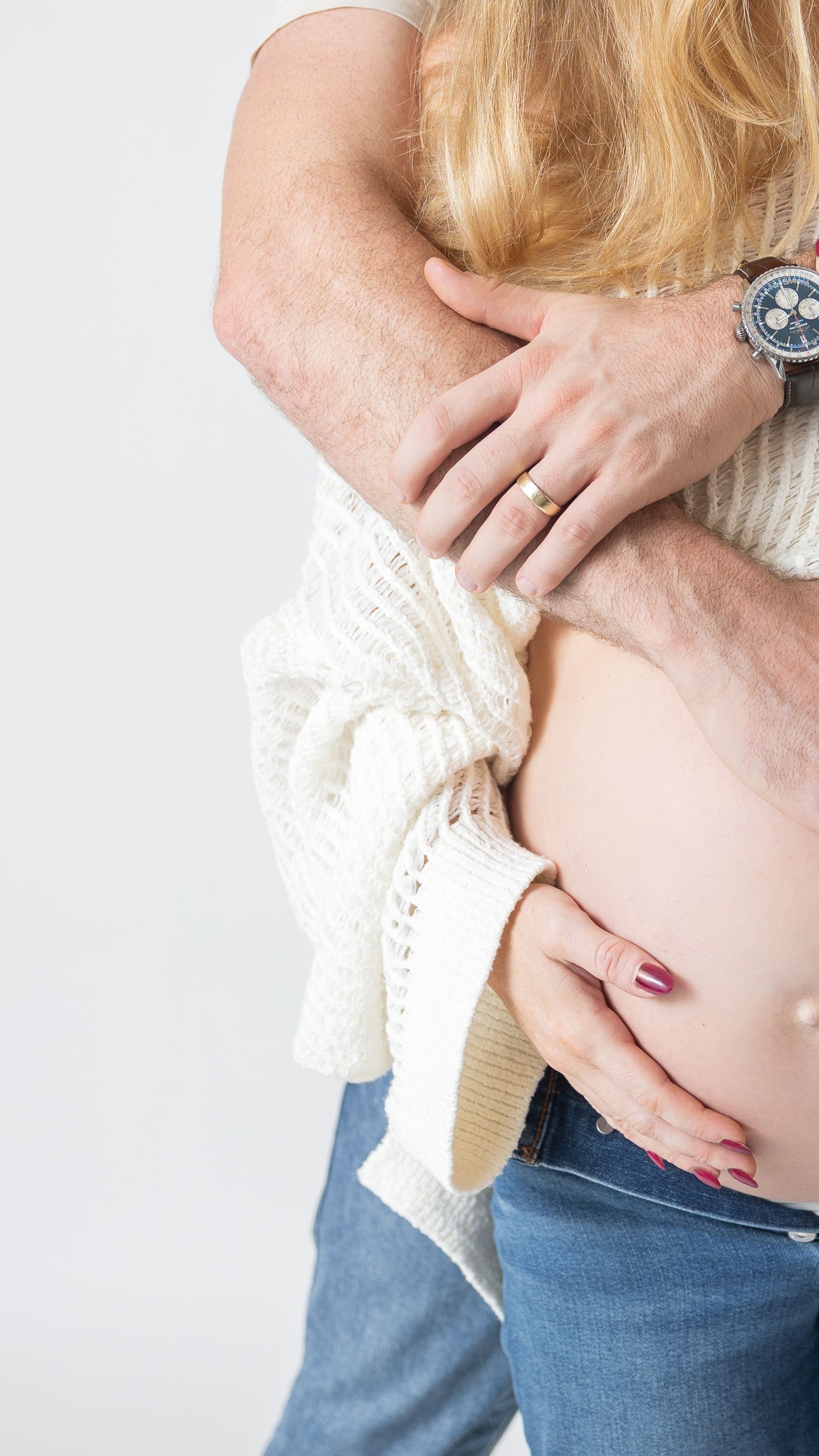 Intimate maternity portrait showing hands cradling baby bump with lace details.