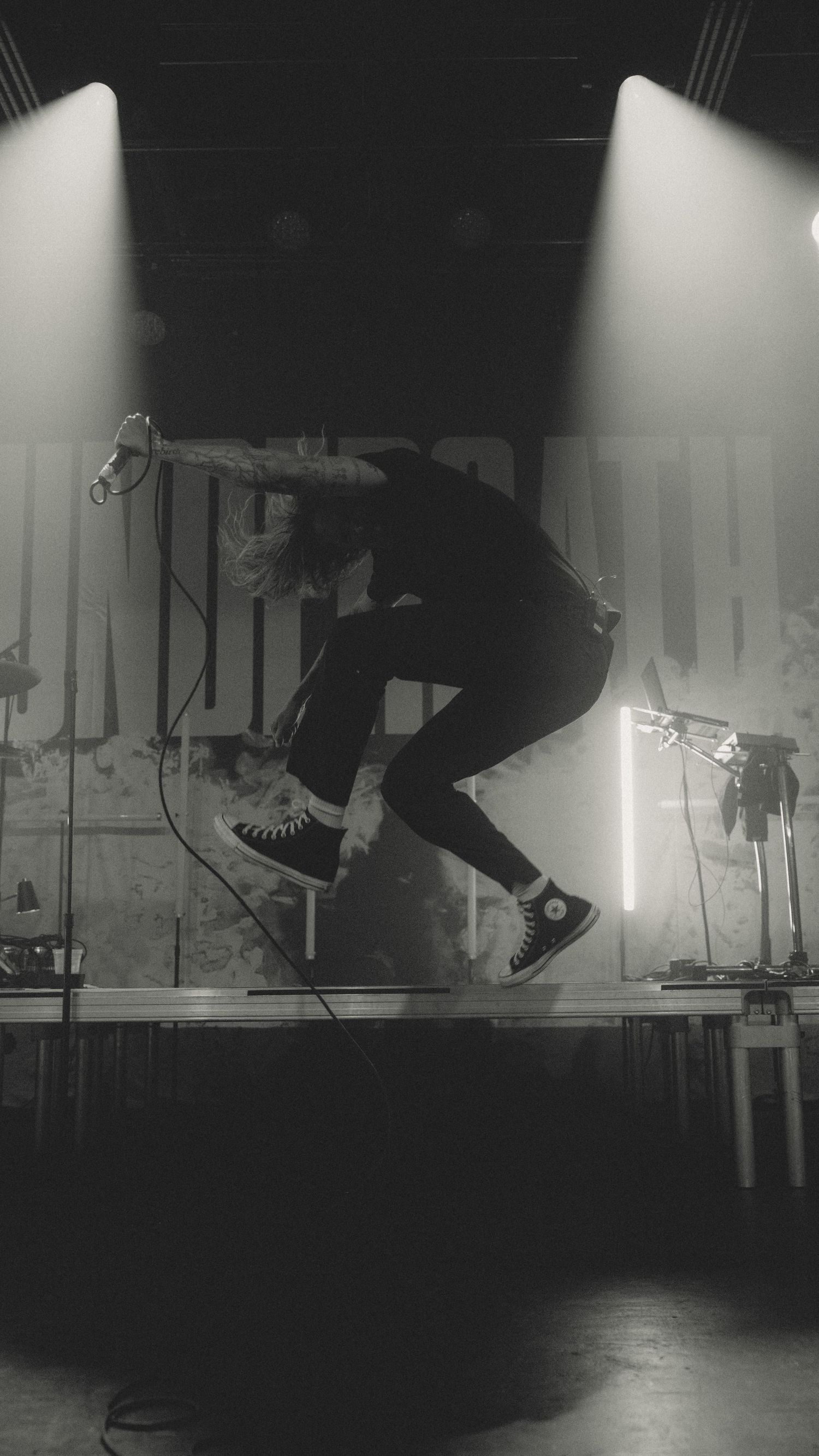 Dynamic black and white photo of performer jumping on stage under dramatic spotlights.