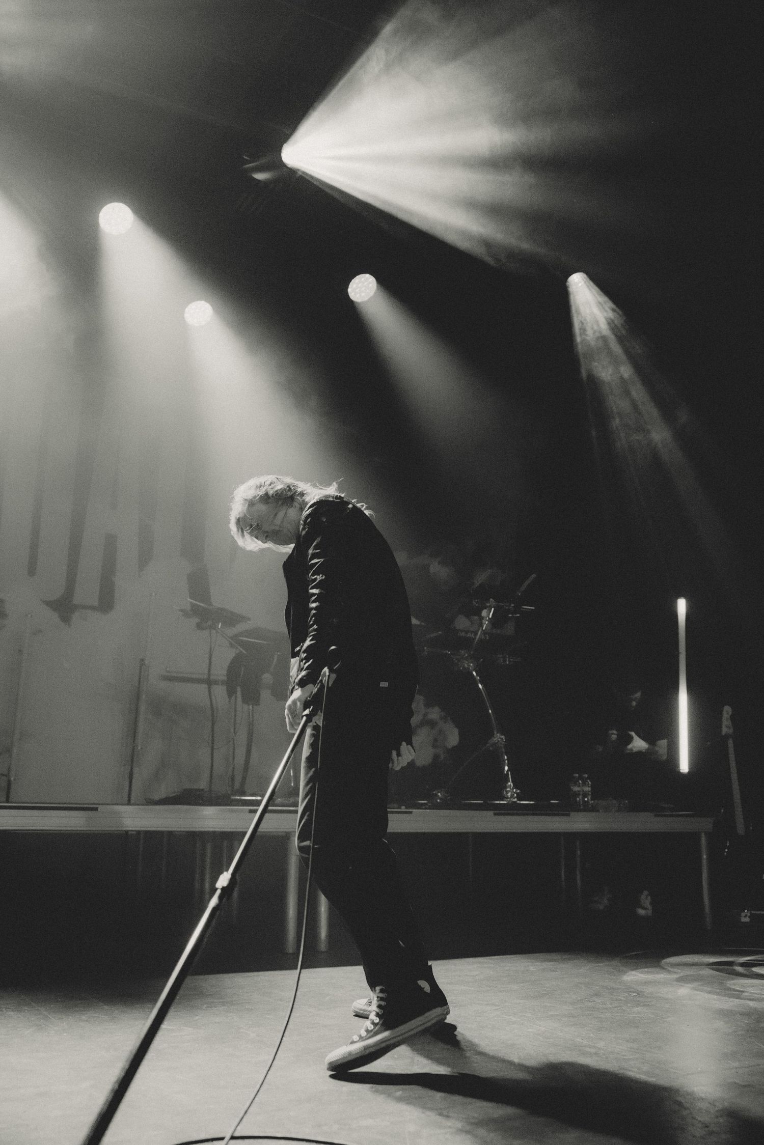 Dramatic black and white stage photo of performer silhouetted under bright spotlights.