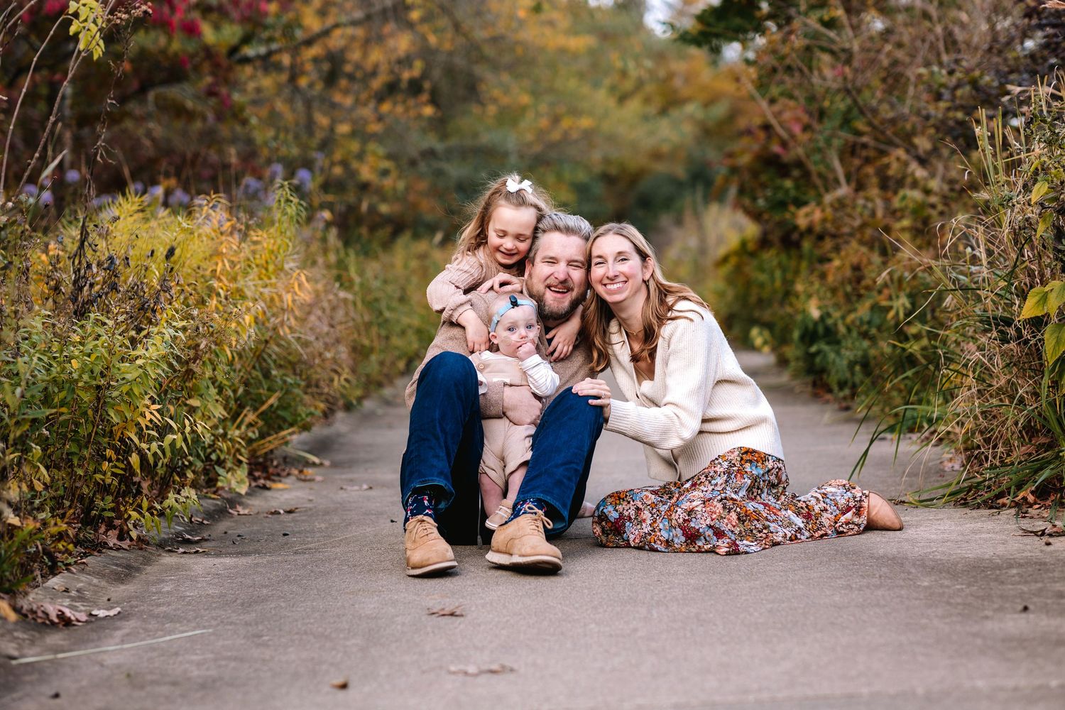 Family of four sitting together on garden path surrounded by autumn foliage.