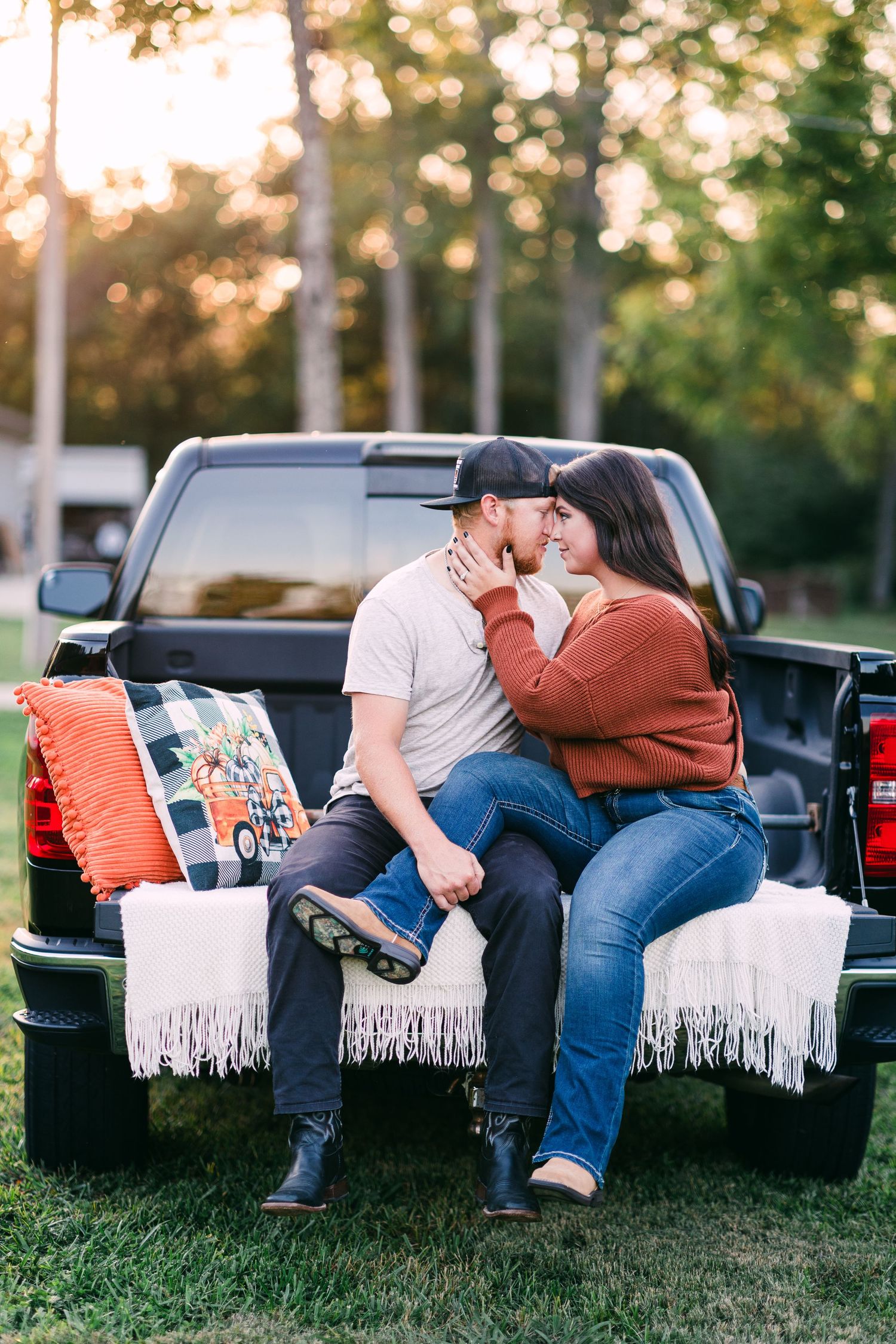 An engaged couple shares a kiss while sitting on a decorated truck tailgate at golden hour.