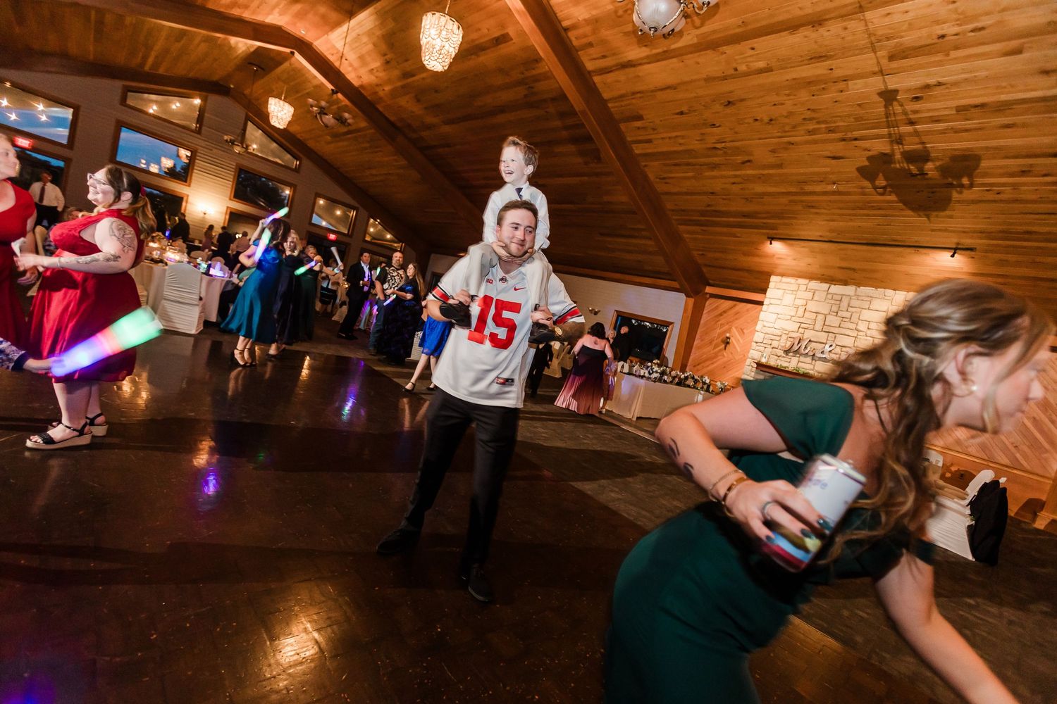 Energetic wedding reception dance floor with guests in colorful attire and a child on shoulders at Lake Lyndsay.