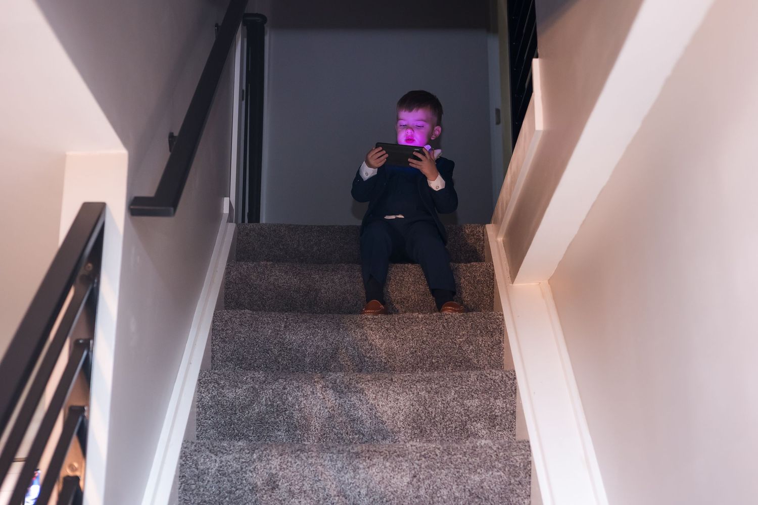 Young child sitting on carpeted stairs illuminated by a glowing phone screen.