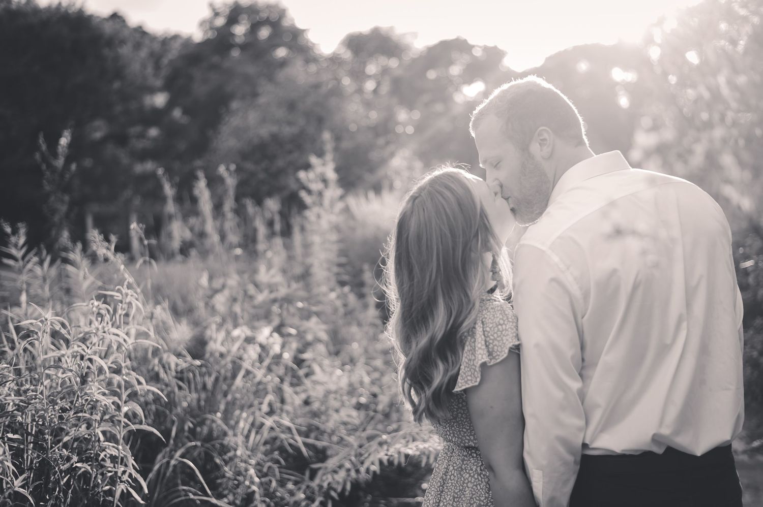 Black and white photo of couple sharing tender moment among wildflowers in a sunlit garden.