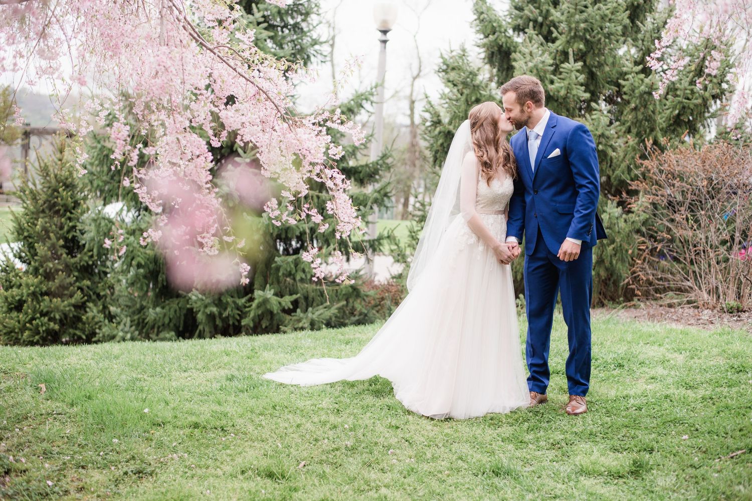 Bride and groom sharing tender moment under pink cherry blossom tree in spring garden.