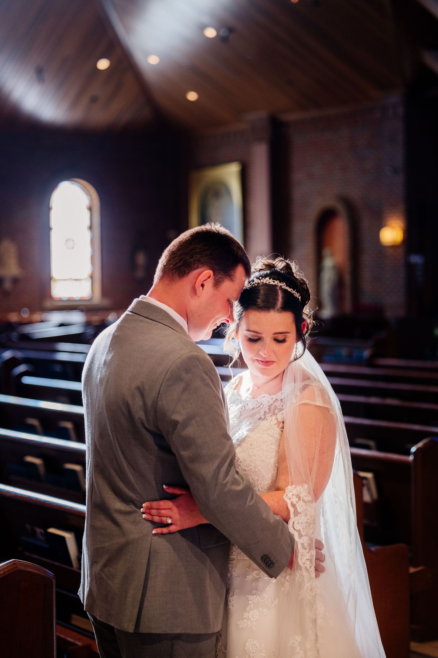 Bride and groom share an intimate moment together inside a warmly lit wooden church on their wedding day.