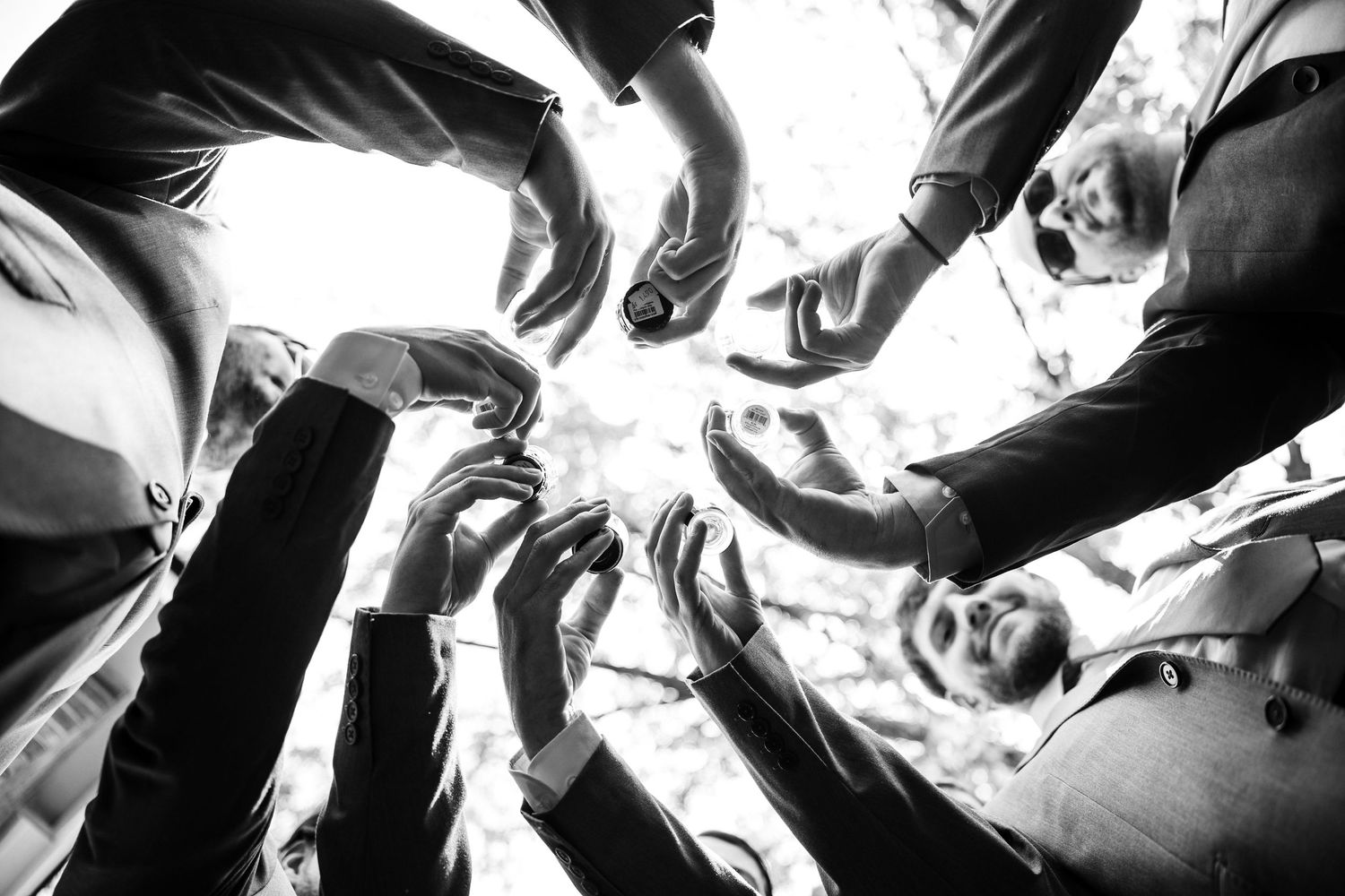 Groomsmen huddle together in a circle from below, raising hands in a team gesture at a wedding.