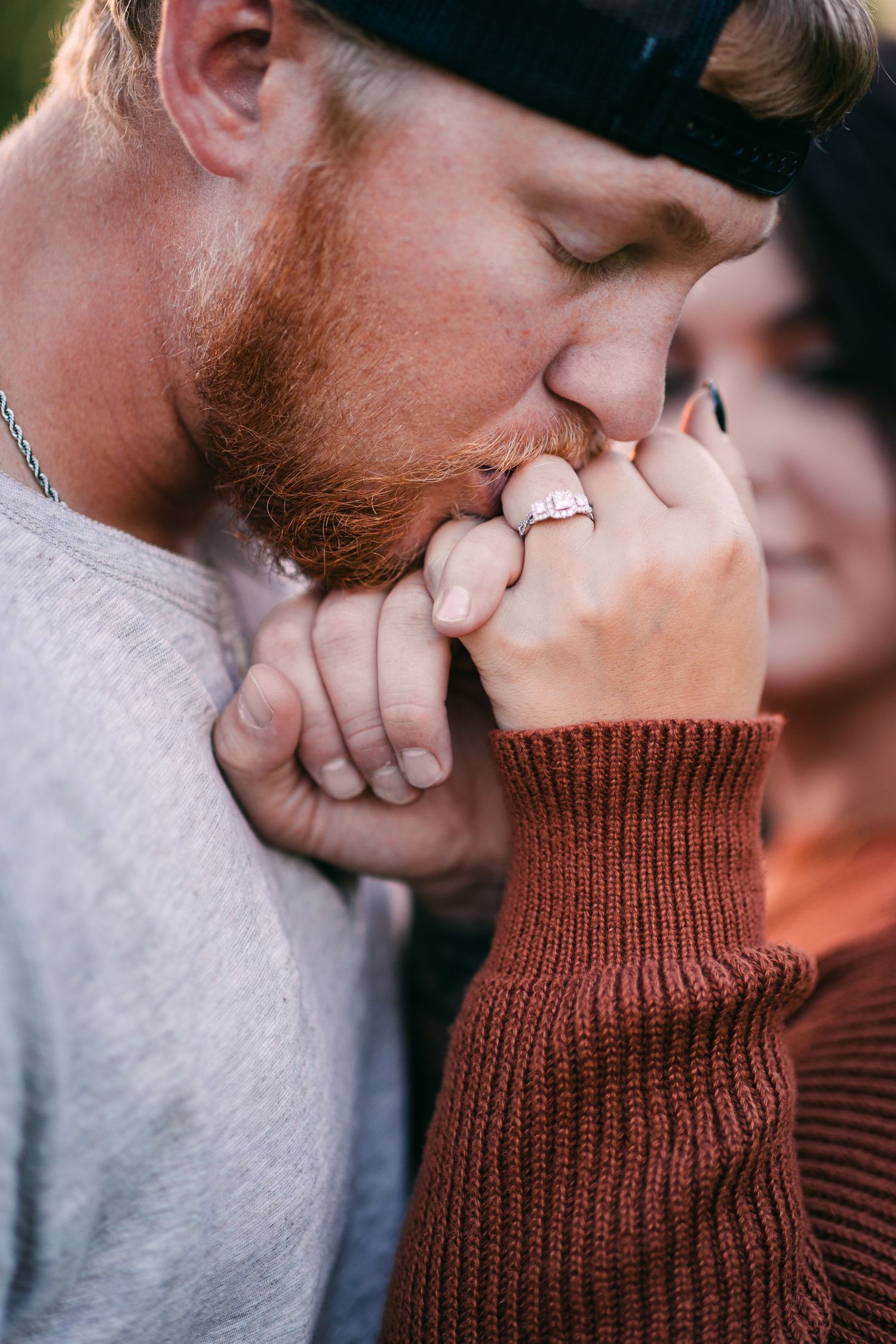 A bearded man tenderly kisses his partners hand showing off her diamond engagement ring.