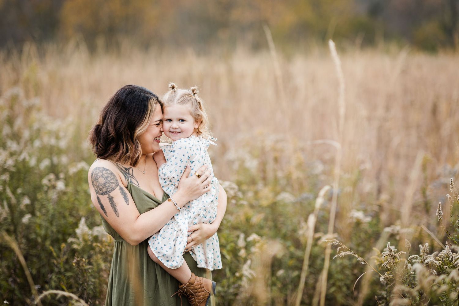 Mother in green dress embracing toddler daughter in golden meadow.