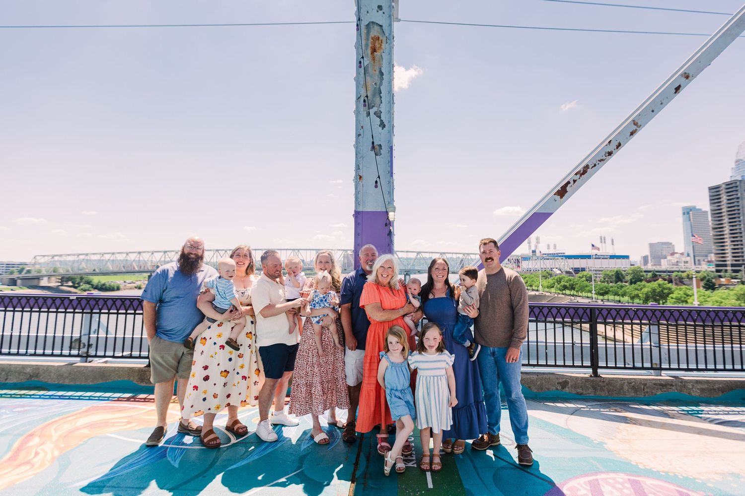 A large extended family group poses together on a colorful bridge on a sunny summer day.