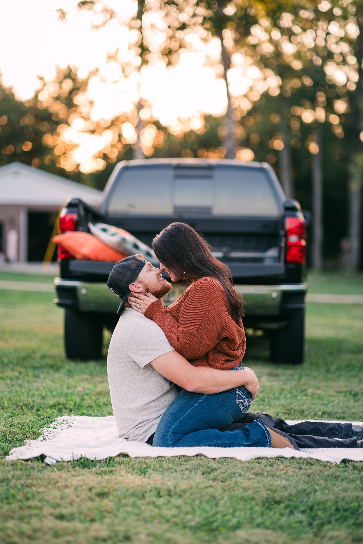 A couple sits intimately on a blanket in front of a pickup truck during a beautiful golden sunset.