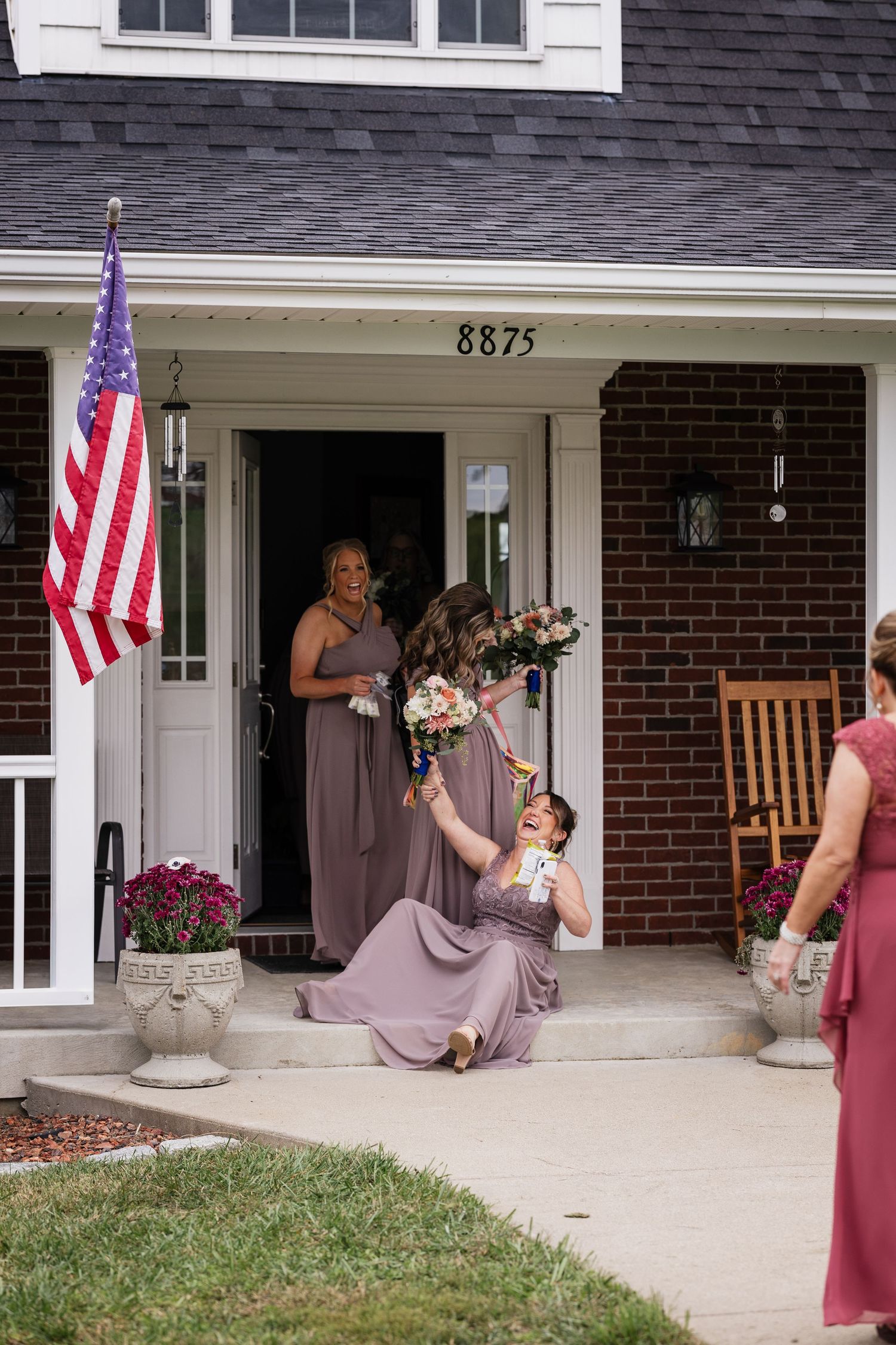 Bridesmaids in mauve gowns celebrating on front porch steps of brick home.