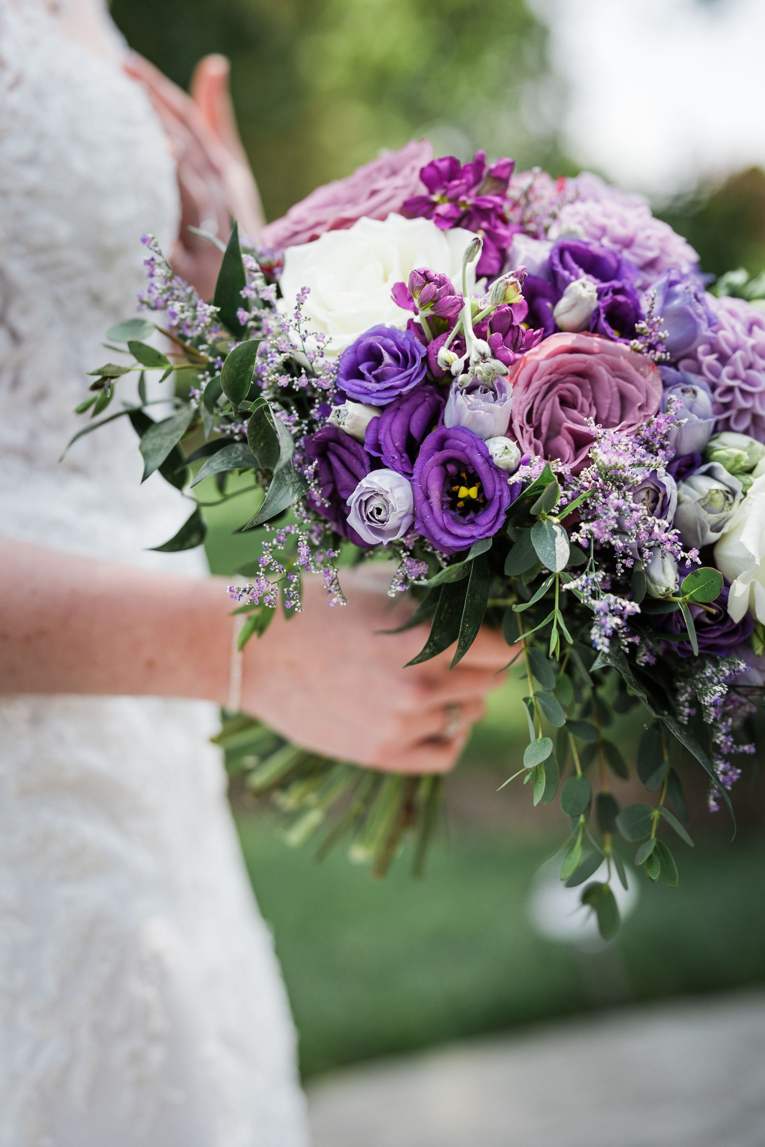 Bride holds a stunning purple and white wedding bouquet with roses, lisianthus, and greenery.