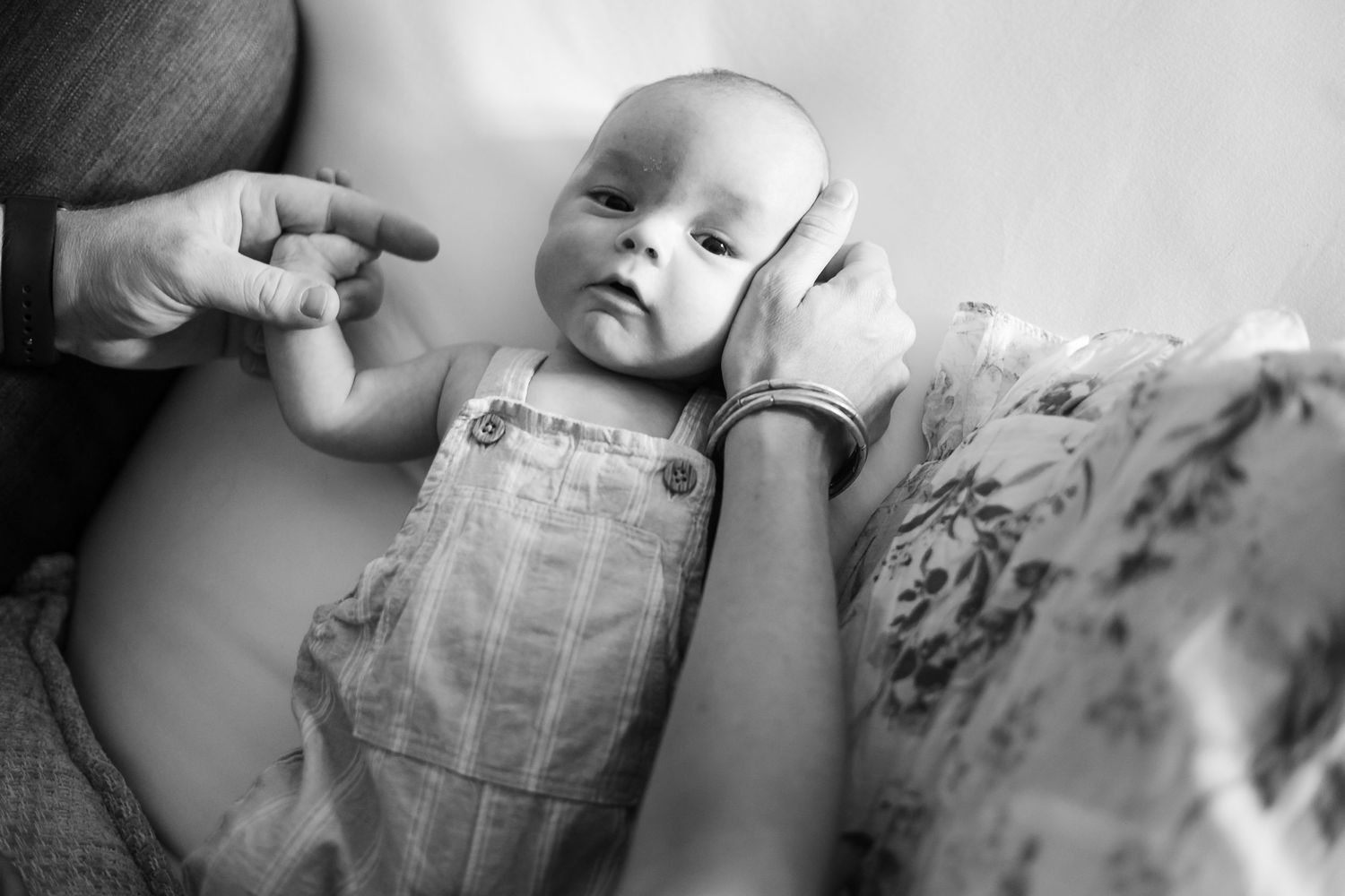 Black and white close-up of a newborn baby in overalls lying on a floral blanket.